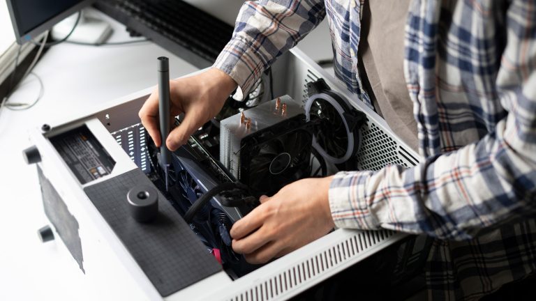 Grafikkarte defekt Eine Person steht vor einem geöffneten PC-Gehäuse und führt mit einem Werkzeug eine Reparatur durch.