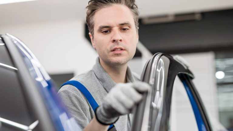Gummidichtungen pflegen Eine Person in einem Blaumann fährt mit dem Zeigefinger die Gummidichtung einer geöffneten Autotür ab.