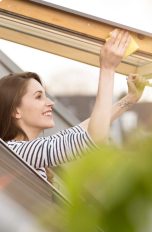 Eine Person reibt mit einem gelben Schwamm an den Rändern eines geöffneten Dachfensters entlang.