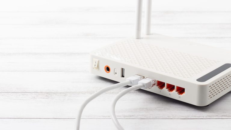 Router einrichten Blick auf die Rückseite eines weißen WLAN-Routers, in den zwei Kabel führen.