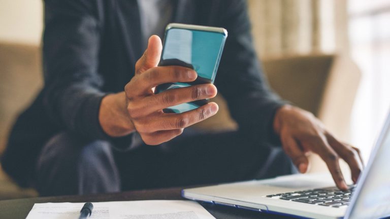 Datenrettung Eine Person tippt mit einer Hand auf einem Laptop und hält in der anderen ein Smartphone.