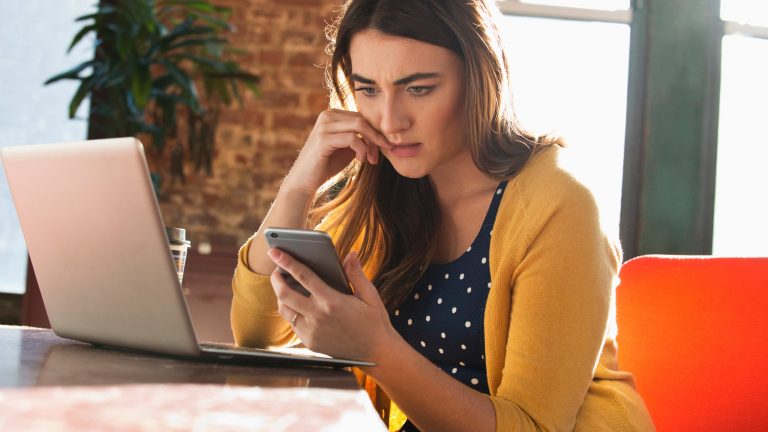 Datenrettung Eine Person sitzt mit ihrem Smartphone in der Hand vor einem Laptop.