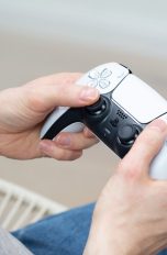 Eine Person hält einen weißen DualSense-Controller in der Hand.