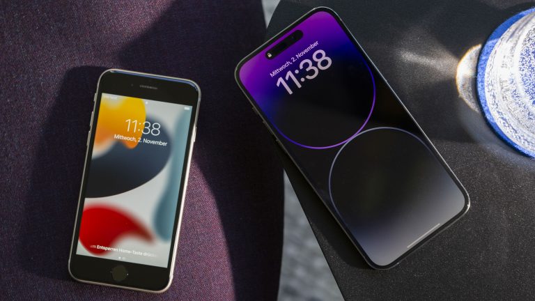 Ein iPhone SE und ein iPhone 14 Pro Max liegen mit eingeschaltetem Bildschirm nebeneinander, um deren Unterschiede hervorzuheben. iPhone 14 Pro Max vs. iPhone SE