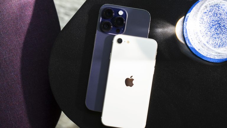 Auf einem schwarzen Tisch liegen ein iPhone 14 Pro Max und ein iPhone SE übereinander, um deren Größenunterschied und die Unterschiede bei den Kameras zu demonstrieren. iPhone 14 Pro Max vs. iPhone SE