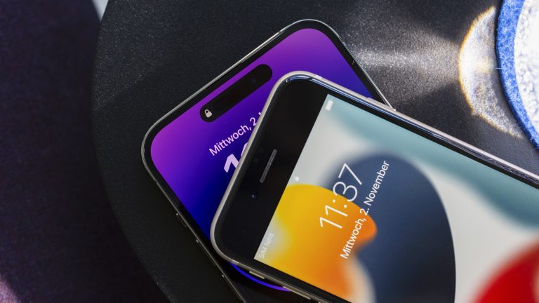 Ein iPhone SE und ein iPhone 14 Pro Max liegen mit eingeschaltetem Bildschirm übereinander, um den Unterschied zwischen dem alten Design des SE und der neuen Dynamic Island des 14 Pro Max darzustellen. iPhone 14 Pro Max vs. iPhone SE