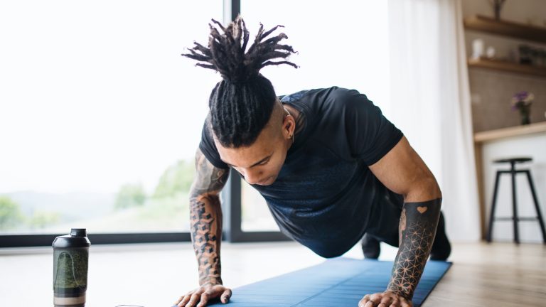 kostenlose Fitness Apps Eine Person macht Zuhause Liegestützen auf einer Yoga-Matte. Neben ihr liegt ein Smartphone.