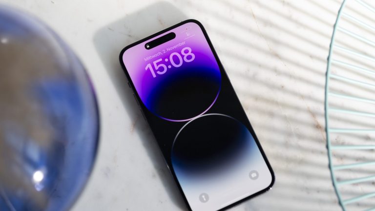 Auf einem weißen Marmortisch liegt ein iPhone 14 Pro, auf dem ein Sperrbildschirm zu sehen ist. iPhone 14 Pro Max Always On Display