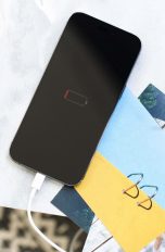 Ein leeres iPhone liegt auf einigen Zetteln und Postkarten. Auf dem Display ist eine leere Batterie zu sehen.