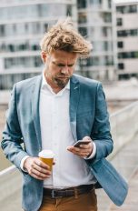 Eine Person mit Kaffeebecher in der Hand spaziert und schaut dabei auf ihr Smartphone.