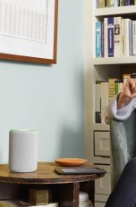 Eine Person sitzt an einem Kaffeetisch, auf dem ein smarter Lautsprecher steht.