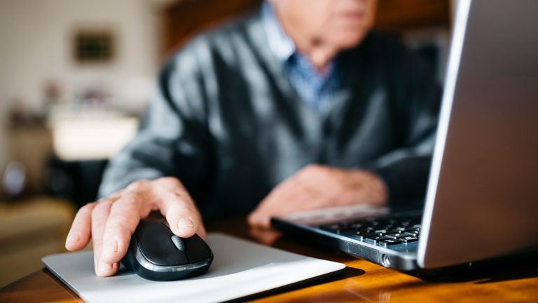 Eine Person sitzt vor einem Laptop und bedient eine Maus.