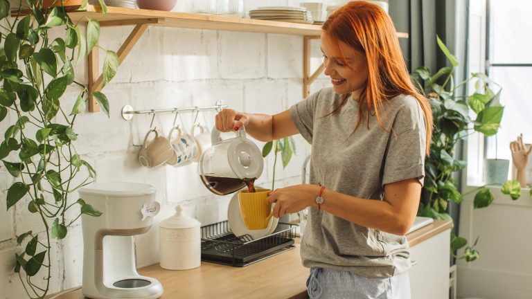 Eine Person gießt etwas Kaffee aus einer Filtermaschine in eine Tasse.