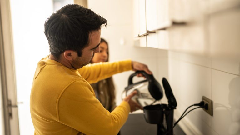 Eine Person gießt etwas Wasser aus einem Wasserkocher in eine Filterkaffeemaschine. Eine Person gießt etwas Wasser aus einem Wasserkocher in eine Filterkaffeemaschine.