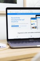 Ein MacBook Pro mit geöffneter OneDrive-Produktseite steht auf einem Tisch.