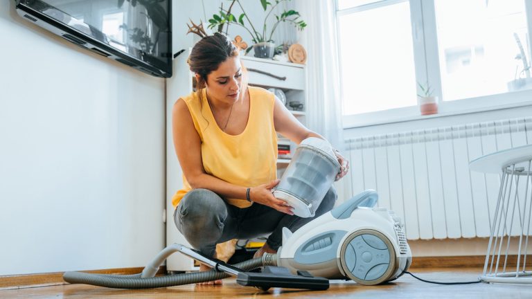 Eine Person hält das Behältnis eines beutellosen Staubsaugers in der Hand.