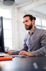 Eine Person sitzt vor einem Rechner in einem Büro.