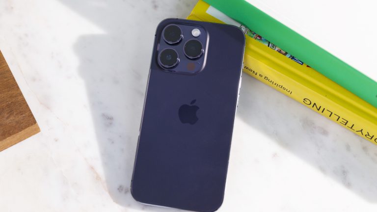 Ein iPhone 14 Pro liegt an Bücher gelehnt auf einer Marmor-Oberfläche.