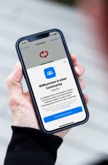 Eine Person hält ein iPhone in der Hand, auf dem die neue Community-Funktion von WhatsApp zu sehen ist.