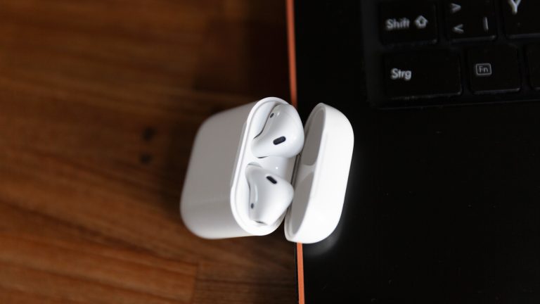 AirPods in ihrem Case liegen neben einem Windows-Laptop. AirPods in ihrem Case liegen neben einem Windows-Laptop.
