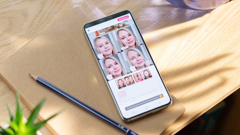 Ein Android liegt auf einem Holztisch. Auf dem Display ist ein Screenshot der App „YouCam Makeup“ zu sehen.