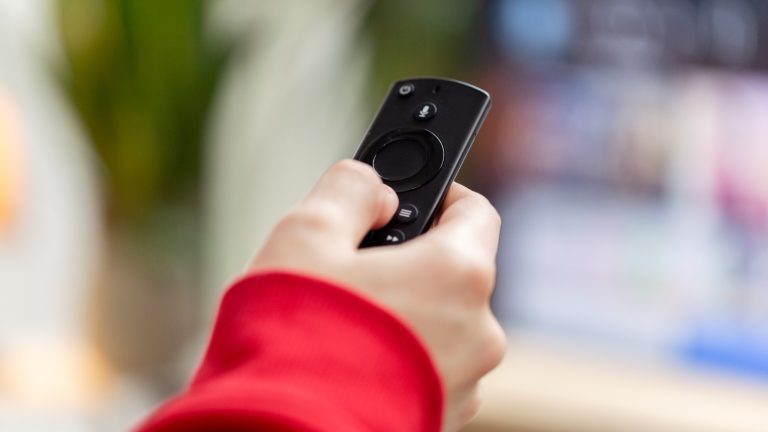 Nahaufnahme einer Fernbedienung für einen Fire TV Stick, die eine Person in der Hand hält.