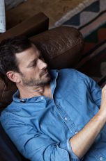 Eine Person liegt auf einem Sofa und bedient ihr Smartphone.