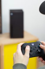 Eine Person sitzt vor einem Fernseher und spielt mit einem Controller in der Hand auf einer Xbox Series X.