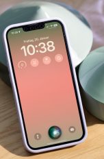 Ein iPhone lehnt an einen Dekotopf. Auf dem Gerät ist der Sperrbildschirm und das leuchtende Siri-Symbol zu erkennen.