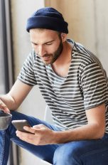 Eine Person mit Kaffeetasse in der Hand schaut auf das Smartphone in der anderen Hand.