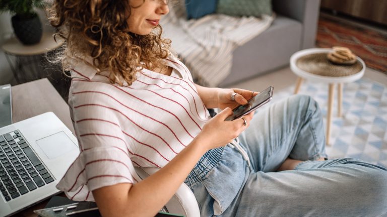 Eine Person sitzt auf einem Schreibtischstuhl und schaut auf ein Smartphone.