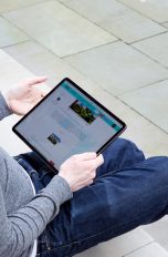 Eine Person sitzt auf einer Treppenstufe und hält ein iPad Pro in der Hand.
