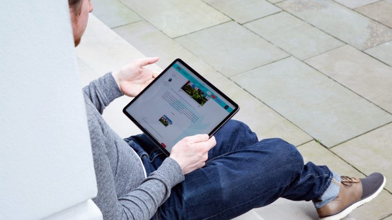 Eine Person sitzt auf einer Treppenstufe und hält ein iPad Pro in der Hand.