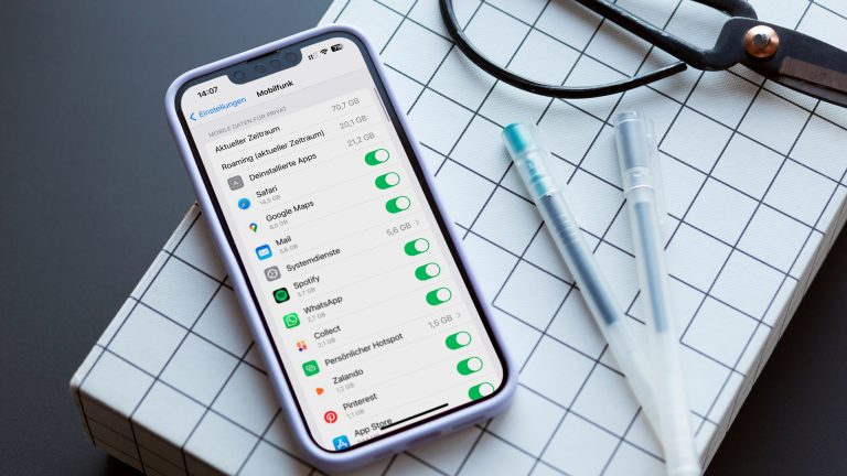 Ein iPhone 13 liegt auf einem karierten Karton. Auf dem Display ist die Mobilfunk-Übersicht geöffnet. Ein iPhone 13 liegt auf einem karierten Karton. Auf dem Display ist die Mobilfunk-Übersicht geöffnet.