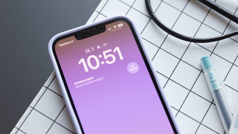 Ein iPhone 13 liegt auf einer Schneidematte. Auf dem Display werden der Sperrbildschirm und einige Symbole in der Statusleiste angezeigt.