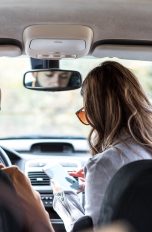 Zwei Personen sitzen in einem Auto. Die eine schaut auf ihr Smartphone.