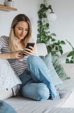Eine Person sitzt auf einem Sofa und schaut auf ihr Smartphone.