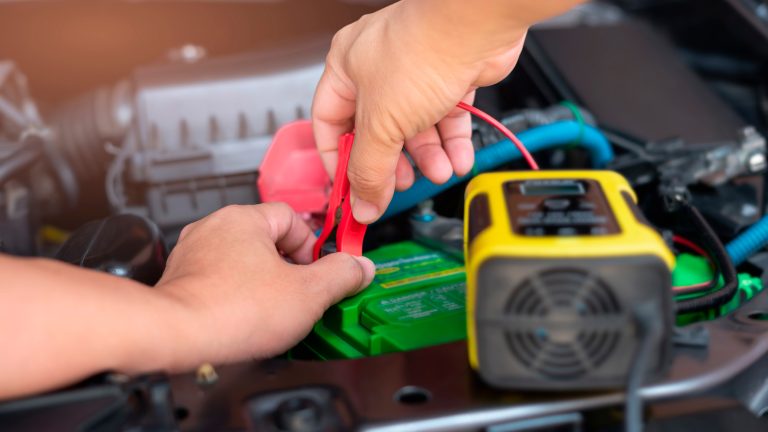 Eine Person steckt ein Batterieladegerät an eine Autobatterie an.