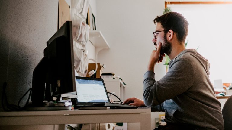 Eine Person sitzt nachdenklich vor einem Laptop und zwei Bildschirmen. Eine Person sitzt nachdenklich vor einem Laptop und zwei Bildschirmen.