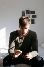 Eine Person sitzt auf einem Bett und bedient ihr Smartphone.