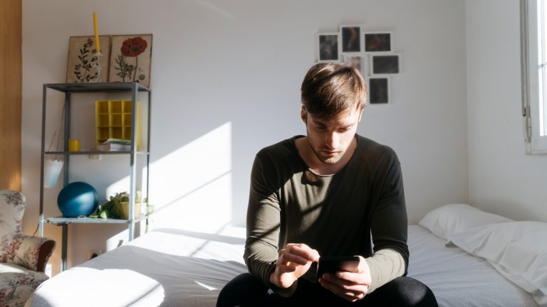 Eine Person sitzt auf einem Bett und bedient ihr Smartphone.
