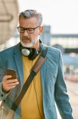 Eine Person blickt auf das Smartphone in ihrer Hand. Um den Hals trägt sie Kopfhörer.