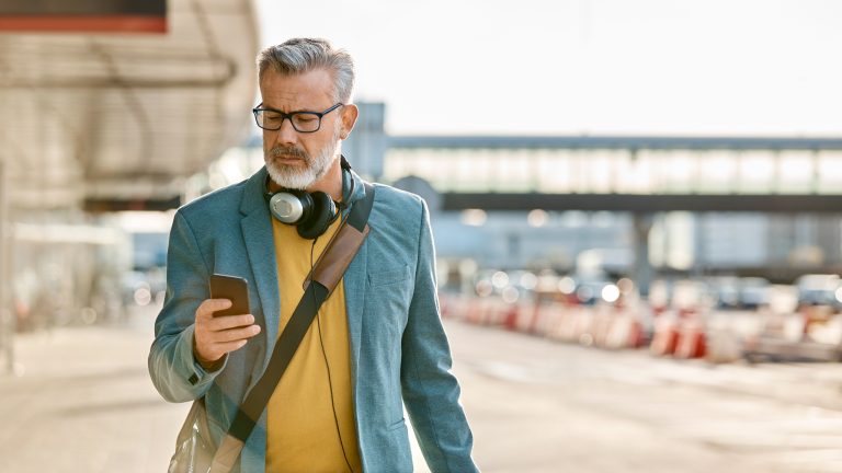 Eine Person blickt auf das Smartphone in ihrer Hand. Um den Hals trägt sie Kopfhörer.