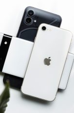 Ein Nothing Phone (1), ein Google Pixel 6a und ein Apple iPhone SE (2022) liegen übereinander gestapelt auf einem weißen Tisch.