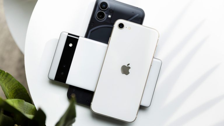 Ein Nothing Phone (1), ein Google Pixel 6a und ein Apple iPhone SE (2022) liegen übereinander gestapelt auf einem weißen Tisch.