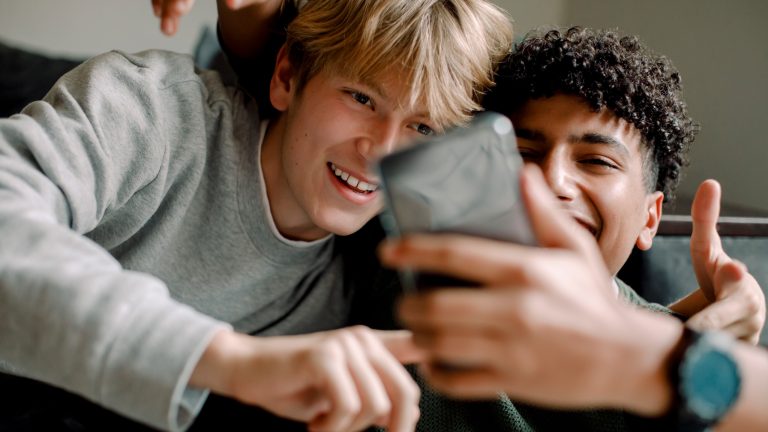 Zwei Personen liegen entspannt auf einem Sofa und albern vor einem Smartphone herum, das eine Person in der Hand hält.