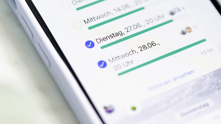 Auf einem Smartphone ist ein WhatsApp-Chat geöffnet. Hier wird per Umfrage-Funktion ein Veranstaltungsort auserkoren.