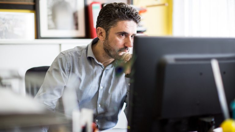 Eine Person sitzt nachdenklich an einem Schreibtisch vor einem Bildschirm.