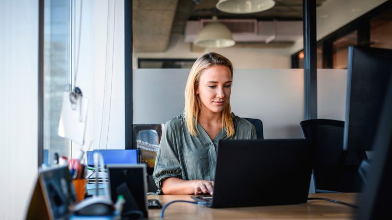 Eine Person sitzt in einem Büro vor einem Windows-Laptop.