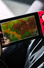 Eine Person hält eine Nintendo Switch in der Hand und spielt ein Spiel darauf.